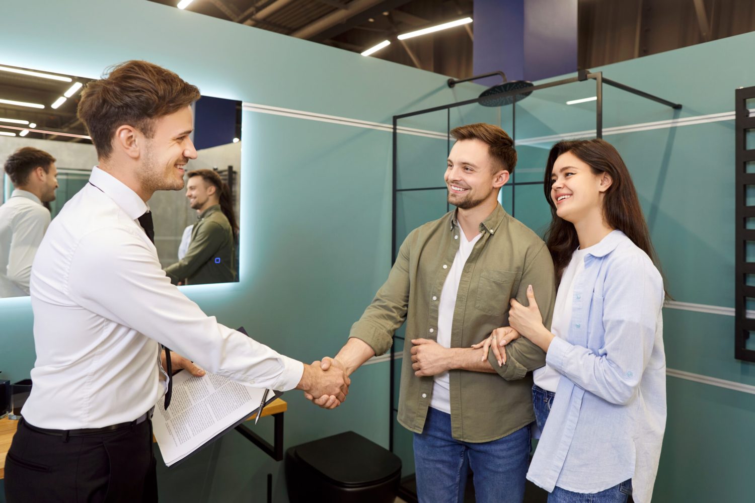 Plumbing Store Salesman Shaking Hands With Couple In a plumbing store, a salesman shakes hands with a couple in agreement. Surrounded by bathroom hardware and water-related home products, the shop fosters trust and customer satisfaction.